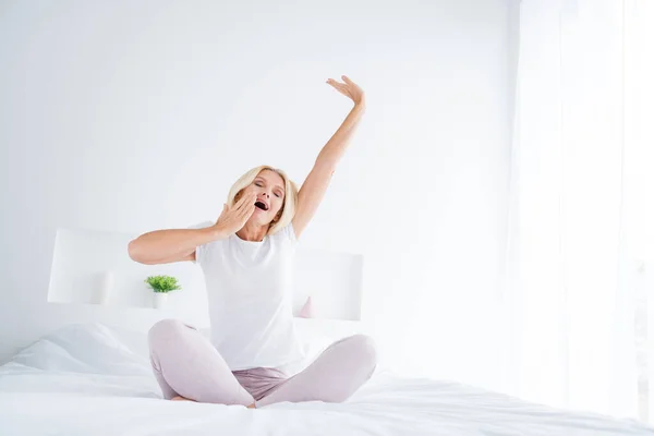 Retrato de ella ella agradable atractiva encantadora bastante soñolienta somnolienta mujer mayor sentada en la cama estiramiento bostezo despertar en la luz moderna habitación interior blanca plana apartamento hotel interior — Foto de Stock