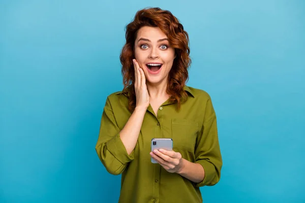 Verbaasde positieve vrouw onder de indruk dat ze honderd sociale netwerk volgers abonnees smartphone touch hand gezicht schreeuwen wow omg dragen goed kijken kleding geïsoleerde blauwe kleur achtergrond — Stockfoto