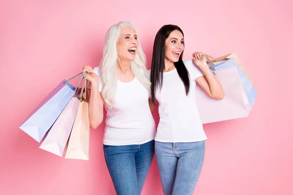 Φωτογραφία από αστεία ηλικίας και δύο νεαρές κυρίες συγγενείς κατέχουν πολλά πακέτα ψώνια μαζί γέλιο δυνατά καλύτερη μέρα φορούν λευκό t-shirts τζιν απομονωμένο παστέλ ροζ χρώμα φόντο — Φωτογραφία Αρχείου