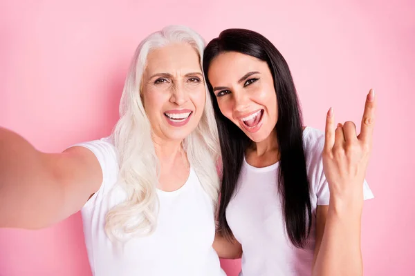 Närbild foto av glada äldre mor ung dotter gör selfies bästa vänner rolig grimma visar finger horn bära vita t-shirts isolerad pastell rosa färg bakgrund — Stockfoto