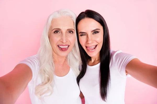 Foto de primer plano de la alegre anciana madre joven hija damas haciendo selfies mejores amigos divertidos muecas expresiones faciales usan camisetas blancas aisladas pastel color rosa fondo — Foto de Stock