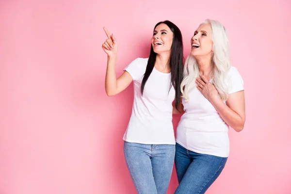 Foto av glada vackra vackra mor ung dotter damer tillbringa tid tillsammans se roliga killar direkt finger skrattar bära vita t-shirts jeans isolerade pastell rosa färg bakgrund — Stockfoto