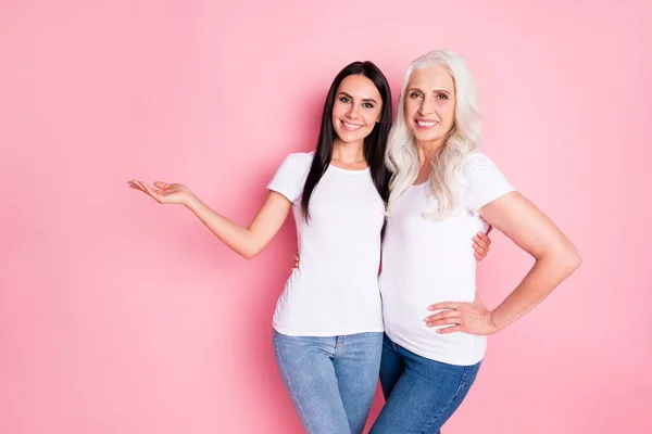 Foto de perfil de la madre bastante vieja joven hija damas abrazo celebración novedad producto en brazo abierto desgaste casual blanco camisetas aisladas pastel rosa color fondo — Foto de Stock