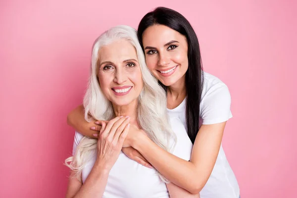 Foto di bella vecchia madre giovane figlia due signore buon umore abbracci a cavalluccio generazione amore comfort indossare casual bianco t-shirt isolato pastello colore rosa sfondo — Foto Stock