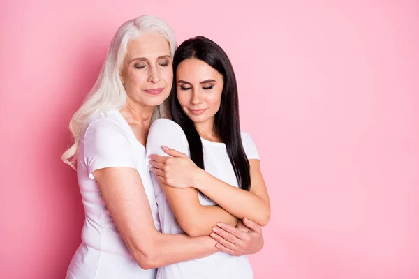 Фото очаровательной матери молодой дочери две дамы поколения обнимать руки уютно, наконец, вместе глаза закрыты носить повседневные белые футболки изолированные пастельно-розовый цвет фона — стоковое фото