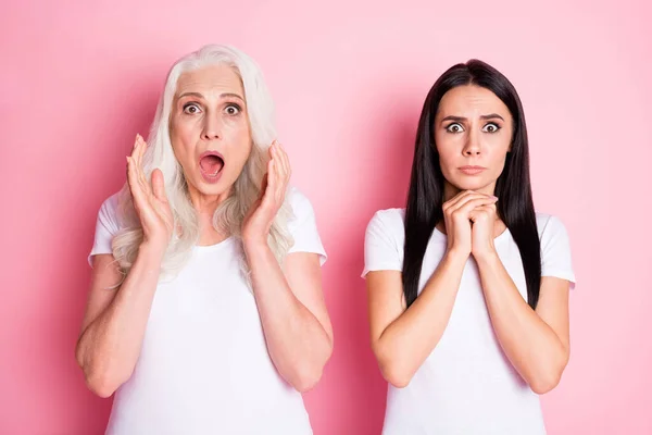 Photo of pretty old mother young daughter two ladies bad mood listen unexpected awful sad news not believe eyes wear casual white t-shirts isolated pastel pink color background