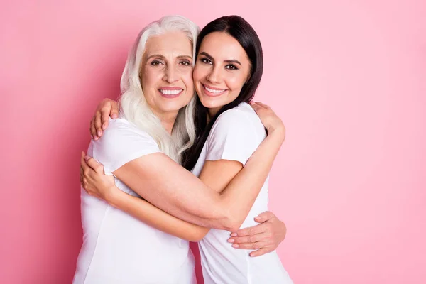 Foto de la encantadora madre anciana joven hija bonita dos señoras abrazando a los mejores amigos acogedores finalmente juntos usan camisetas blancas casuales aisladas pastel color rosa fondo — Foto de Stock