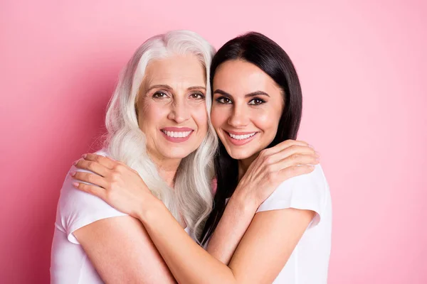 Foto av charmiga äldre mor ung vacker dotter två damer gott humör krama bästa vänner genom åren bära casual vita t-shirts isolerade pastell rosa färg bakgrund — Stockfoto