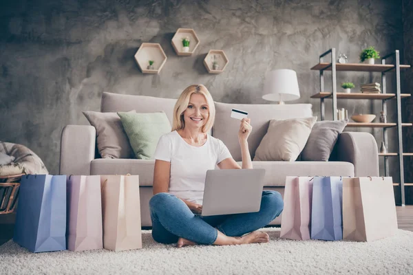 Retrato de ella ella agradable atractiva encantadora alegre señora madura segura sentada en la alfombra usando el ordenador portátil comprar ropa de cosas nuevas en el loft industrial moderno casa de apartamentos de estilo interior — Foto de Stock