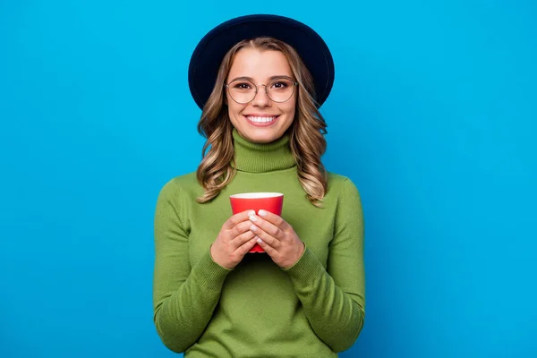 Photo of attractive cheerful pretty lady hold hot fresh beverage mug hands good mood wear specs retro vintage hat casual green turtleneck isolated blue color background — Stock Photo, Image