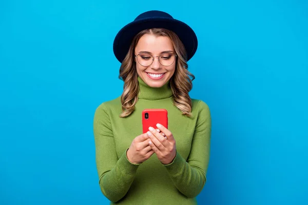 Foto de alegre engraçado encaracolado senhora segurar telefone popular blogger escrita novo post estudante tema desgaste especificações chapéu casual verde gola alta isolado azul cor fundo — Fotografia de Stock