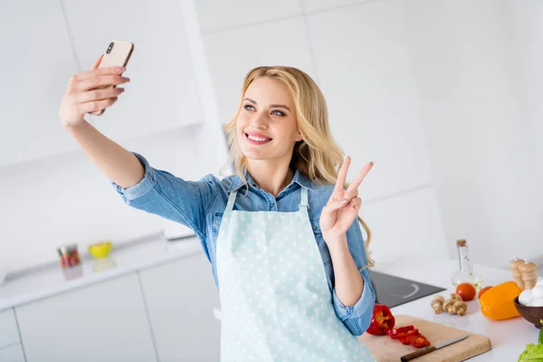 Foto van mooie huisvrouw hold telefoon maken selfie show v-teken symbool opname video vlog blog koken smakelijk veganistisch maaltijd quarantaine verblijf thuis tijd keuken binnen — Stockfoto