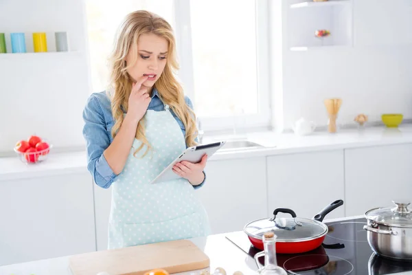 Foto van mooie huisvrouw dame houden digitale tablet zoeken recept internet denk dat ze verkeerd ingrediënt ontbijt kok familie diner dragen schort shirt stand moderne keuken binnen toe te voegen — Stockfoto