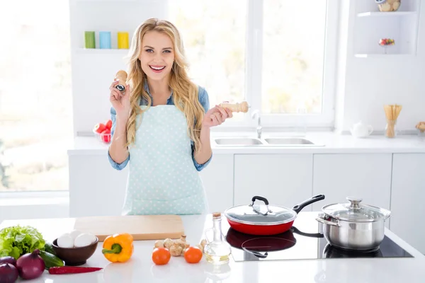 Foto de bela e engraçada dona de casa loira segurar duas garrafas de especiarias bom humor tempo de café da manhã dança e cozinhar saborosa refeição animado desgaste avental camisa stand cozinha moderna dentro de casa — Fotografia de Stock