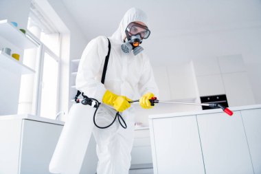 Low angle view photo of focused guy worker hold sprayer latex gloves gas glasses hands spray steam decontaminate ncov epidemic spreading in house kitchen indoors clipart