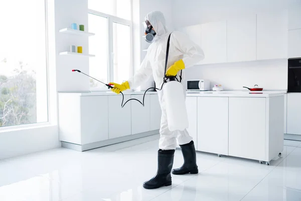 Full body profile side photo of focused guy cleaner in coverall spray sprayer window kitchen whitre surface prevent covid contamination epidemic spreading indoors house