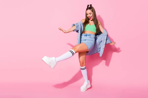 Foto de perfil de cuerpo completo de la señora funky buen humor extendió las manos levantan la pierna de la cadera bailando usar chaqueta de mezclilla verde recorte superior falda desnuda del vientre calcetines de rodilla zapatos aislados pastel de color rosa fondo — Foto de Stock