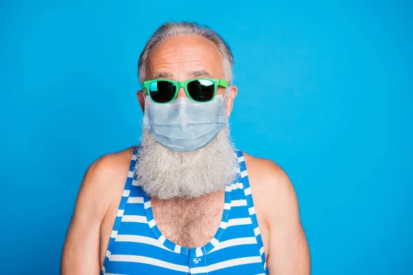 Closeup portrait of attractive funky glad gray haired old man spend leisure pool party in spite of quarantine use protective medical face mask isolated blue background — Stock Photo, Image