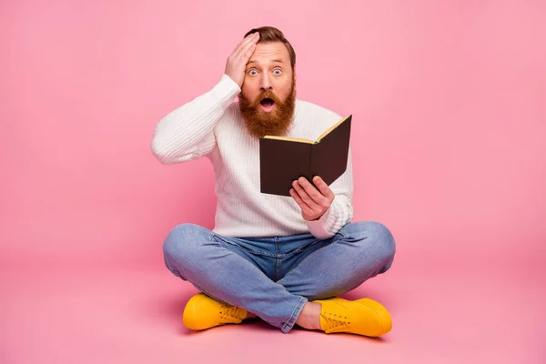 Full size photo astonished guy sit floor legs crossed read paper book impressed unexpected scream touch hand forehead wear jumper sweater bright footwear isolated pastel color background
