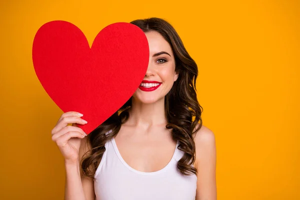 Foto de senhora muito alegre segurar grande papel coração cartão postal escondendo metade da expressão facial 14 fevereiro romance data presente desgaste branco casual singlet isolado cor amarela fundo — Fotografia de Stock