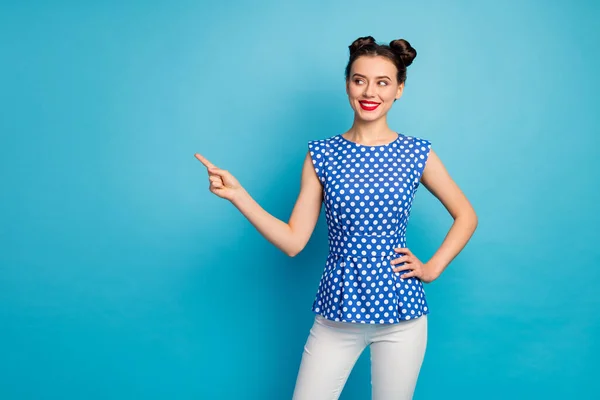 Photo of pretty charming lady directing finger look empty space advising low shopping prices red lips wear dotted blouse shirt white pants isolated blue color background