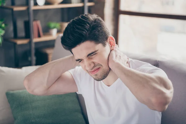 Close-up portrait of his he nice attractive miserable sick guy sitting on divan suffering touching neck pain treatment therapy massage at modern industrial loft brick interior style living-room