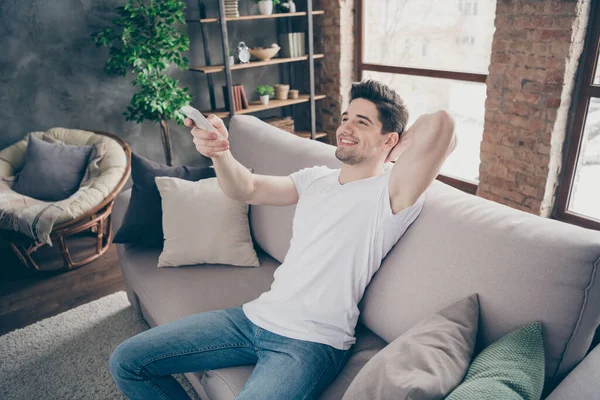 Portrait of his he nice attractive glad confident cheerful cheery muscular virile guy resting switching cool AC mode at modern industrial loft brick interior style living-room