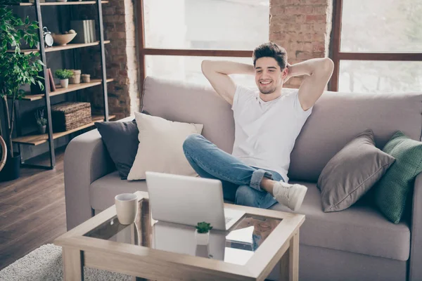 Retrato de su agradable atractivo musculoso alegre alegre chico sentado en diván descansando trabajando remotamente a tiempo parcial en el moderno loft industrial estilo interior sala de estar en el interior — Foto de Stock