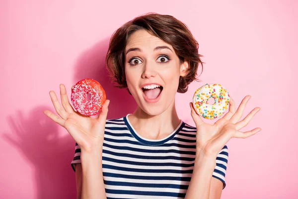 Πορτρέτο του χαρούμενου ενεργητικός κορίτσι θέλουν τρώνε σνακ απολαμβάνουν ζαχαροπλαστικής δείχνουν δύο ντόνατς φορούν καλά ρούχα εμφάνιση απομονώνονται σε παστέλ χρώμα φόντο — Φωτογραφία Αρχείου