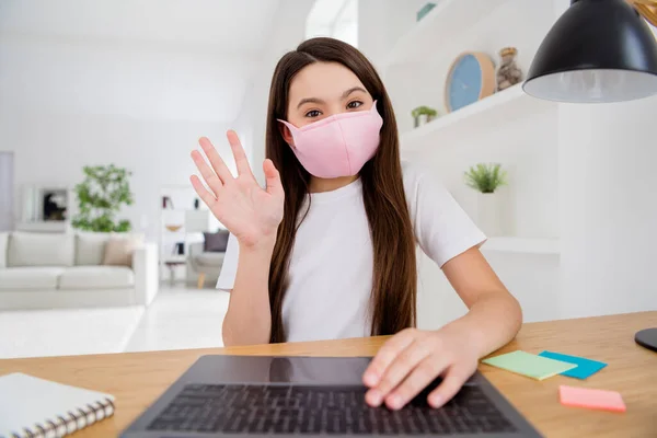 Close-up foto van kleine leerling school dame praten notebook online les video vergadering leraar klasgenoten zeggen hi raise arm zit bureau gebruik gezichtsmasker afstand quarantaine studie huis kamer binnen — Stockfoto