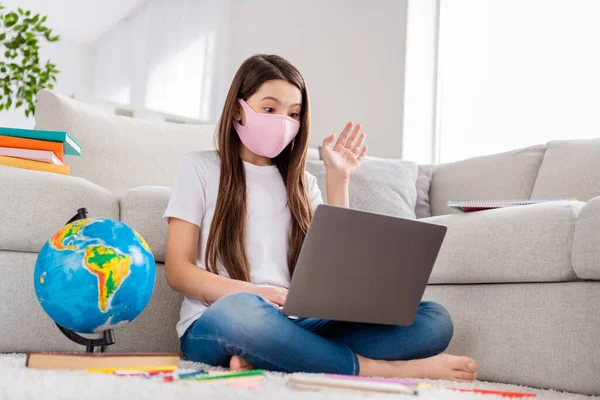 Foto van kleine leerling schoolmeisje notebook laptop verhogen arm weten vraag antwoord leraar online les aardrijkskunde object zitten vloer binnenlandse afstand quarantaine studie veiligheid gezichtsmasker binnen — Stockfoto