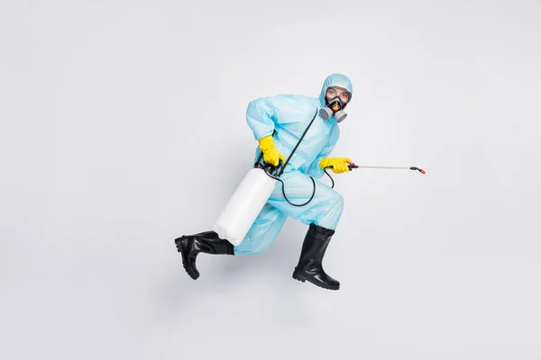 Perfil de tamaño completo lado foto hombre salto carrera uso pulverizador prisa desinfectar casa desgaste traje blanco hazmat amarillo goma látex guantes gafas respiración máscara aislado gris color fondo — Foto de Stock