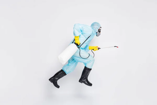 Full body profile side photo man jump run hurry disinfect covid spread house wear white hazmat suit yellow rubber latex gloves goggles use sprayer isolated gray color background