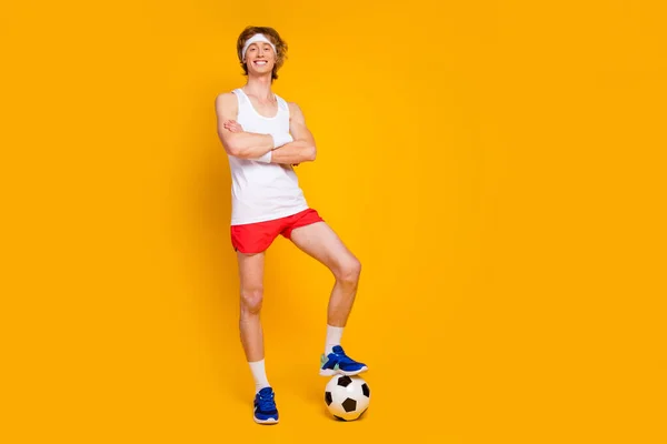 Full length body size view of his he nice attractive cheerful cheery glad guy sportsman folded arms holding leg on ball isolated over bright vivid shine vibrant yellow color background — стоковое фото