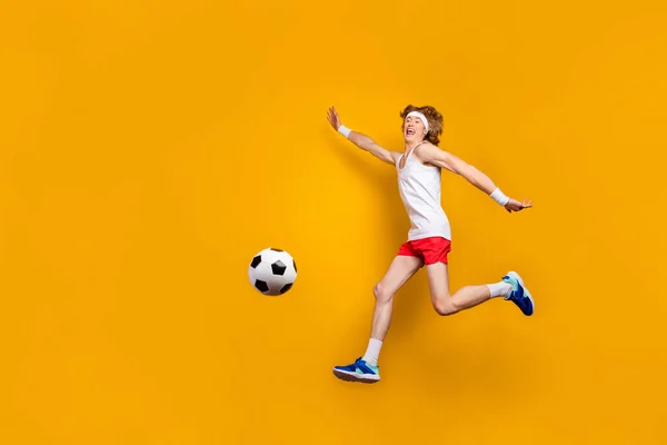 Взгляд в полный рост на его симпатичный, веселый, жизнерадостный, мотивированный парень, прыгающий, играя в футбол, развлекаясь на ярком светящемся ярко-желтом фоне — стоковое фото