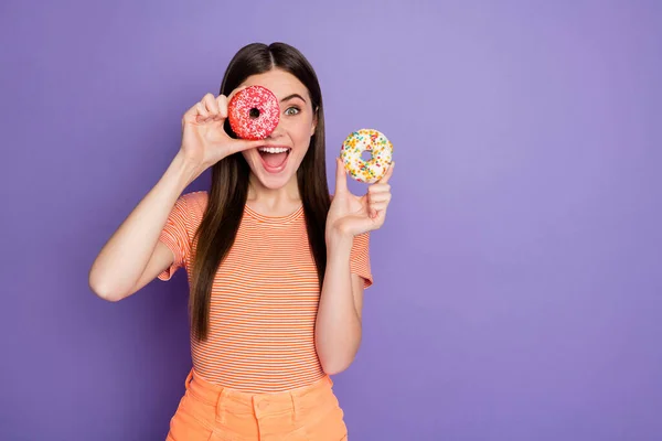 Фото довольно фанки леди длинная прямая прическа держать руку свежие глазурованные пончики, выглядящие как очки носить случайные оранжевые полосатые футболки изолированные пастельно-фиолетовый цвет фона — стоковое фото