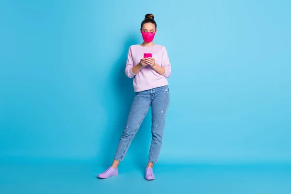 Foto in voller Größe von ziemlich sicher Dame halten soziale Distanz Menschen halten Telefon Hände warten Freunde Treffen tragen Gesichtsmaske Jeans Pullover Schuhe isoliert blaue Farbe Hintergrund — Stockfoto