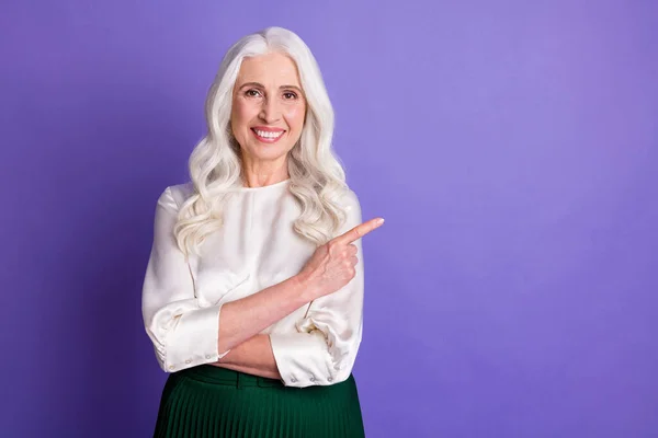 肯定的な陽気な古い女性のポイントインデックス指のコピースペース広告プロモーションへの直接的な方法の肖像は、紫の色の背景に隔離された良い外観のスカートを着用することをお勧めします — ストック写真