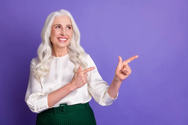 陽気な高齢女性プロモーターポイント指数指コピースペースの肖像は、紫の色の背景に隔離された特定の広告プロモーションの着用スカートを示唆している — ストック写真