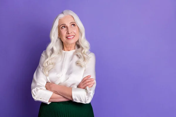 Foto van aantrekkelijke oude witte haren dame glimlachen goed humeur armen gekruist kijk omhoog lege ruimte dromerig dragen witte blouse groen lang midi rok geïsoleerde pastel paarse kleur achtergrond — Stockfoto