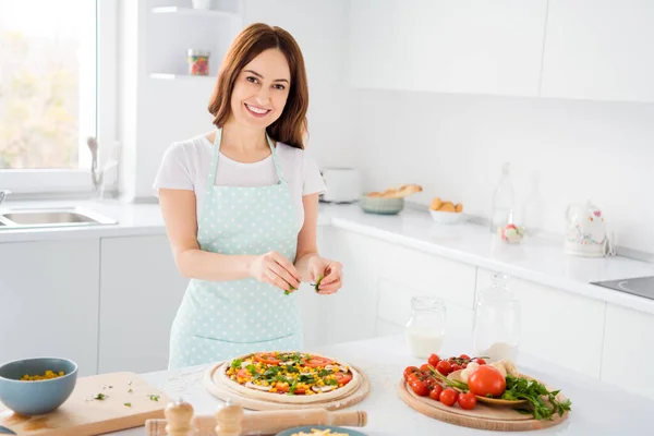 Retrato de positivo encantador menina dona de casa cozinheiro saboroso pizza tempero orégano desgaste pontilhado avental em casa dentro de casa — Fotografia de Stock