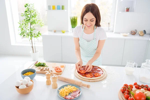 Boven hoge hoek uitzicht foto van positieve vrolijke huisvrouw genieten van koken Italiaanse margarita pizza zet salami rundvlees tomaat plakjes dragen gestippelde schort in huis binnen — Stockfoto