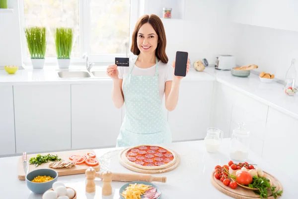 긍정적 인 소녀 요리사가 신용 카드 스마트폰을 들고 있는 모습, 피자 신선 한 재료 배달 피자를 제공하고 있다. — 스톡 사진