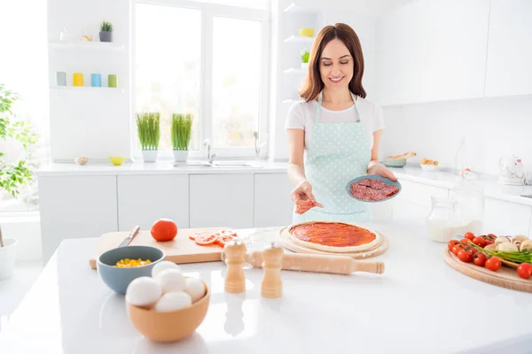 Foto de bela dona de casa alegre desfrutar de hobby cozinhar receita familiar jantar cobertura massa pizza ingredientes desgaste t-shirt avental pé cozinha moderna em casa — Fotografia de Stock