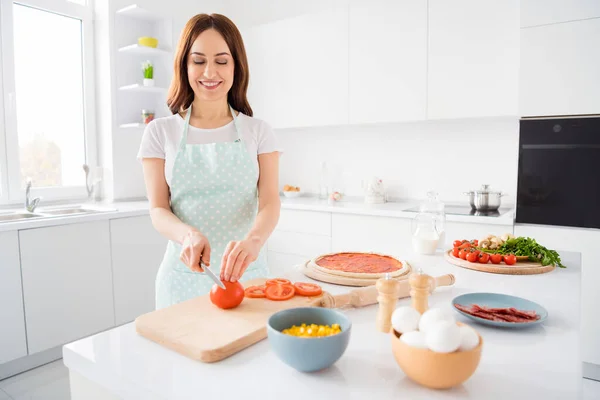 Portret van positieve vrolijke huisvrouw genieten koken junk ongezond voedsel gesneden tomaat snijplank lekker pizza ingrediënt dragen gestippelde schort in keuken huis binnen — Stockfoto