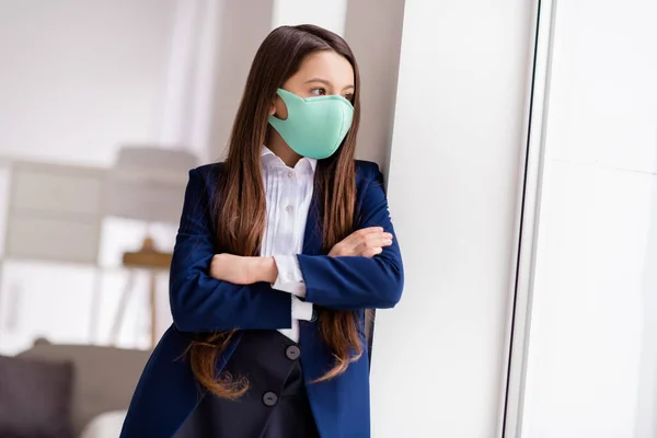 Foto van kleine student schoolmeisje student kijken venster armen gekruist vermist gaan buiten dragen uniform bescherming ademhalingsmasker quarantaine studie woonkamer binnen — Stockfoto