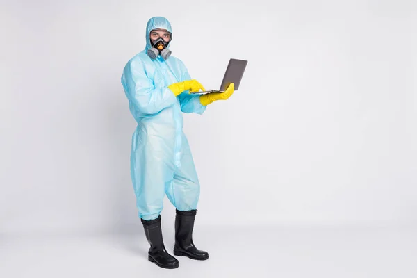 Full length photo man medical worker use laptop work remote search coworking covid protection information wear white suit hazmat yellow latex gloves goggles isolated grey color background — Zdjęcie stockowe