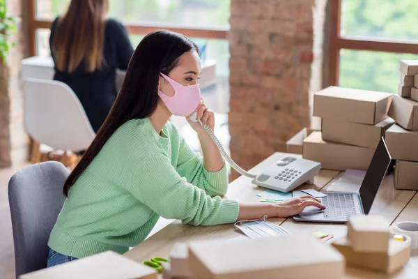 Profile photo of chinese business lady manager organize facial medical masks orders delivery boxes speak landline customer details noting information notebook home office indoors