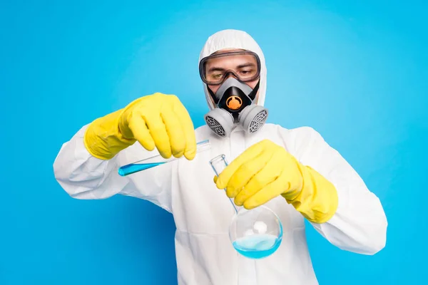 Portret skoncentrowanego chemika wlać sondy płynu covid szczepienia eksperyment nosić biały garnitur hazmat żółty lateks rękawice gogle maska oddechowa odizolowany niebieski kolor tło — Zdjęcie stockowe