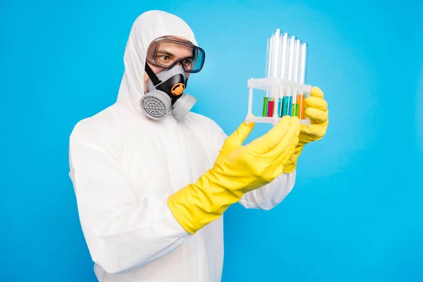 Фото зосередженого вченого чоловік тримає пробірку аналізують рідку майбутню ковадлу19 вакцинації в білому костюмі з маскою для дихання жовті латексні рукавички окуляри ізольовані синій колір фону — стокове фото